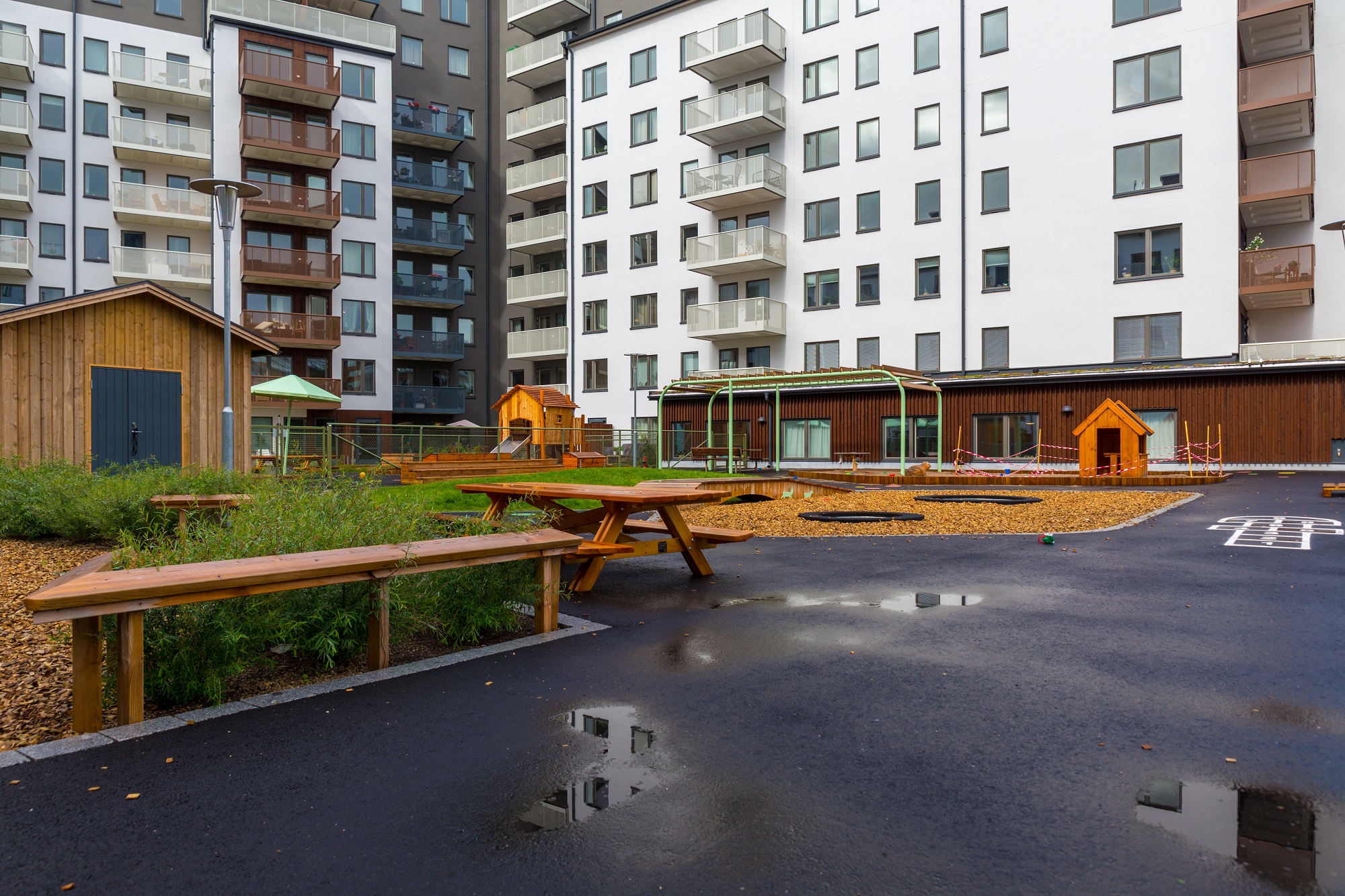 Innergård till flerbostadshus med asfalt, buskar och lekobjekt.