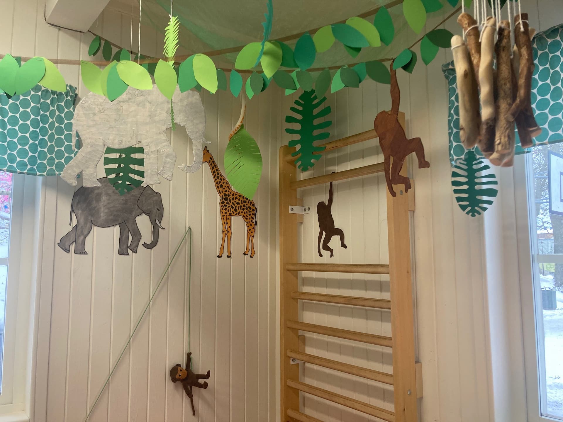 Pappersdjur som elefant, giraff och apor hänger från taket ovanför en ribbstol i ett lekrum.