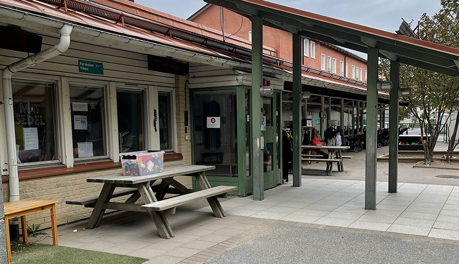Gul tegelbyggnad med grön entré och picknickbord utanför.