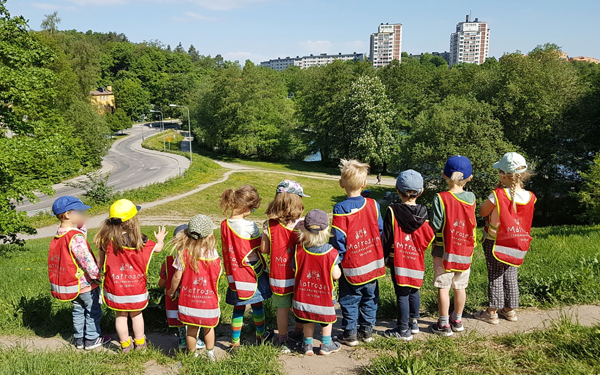 En grupp barn i förskolans västar står på en höjd och ser ut över staden.