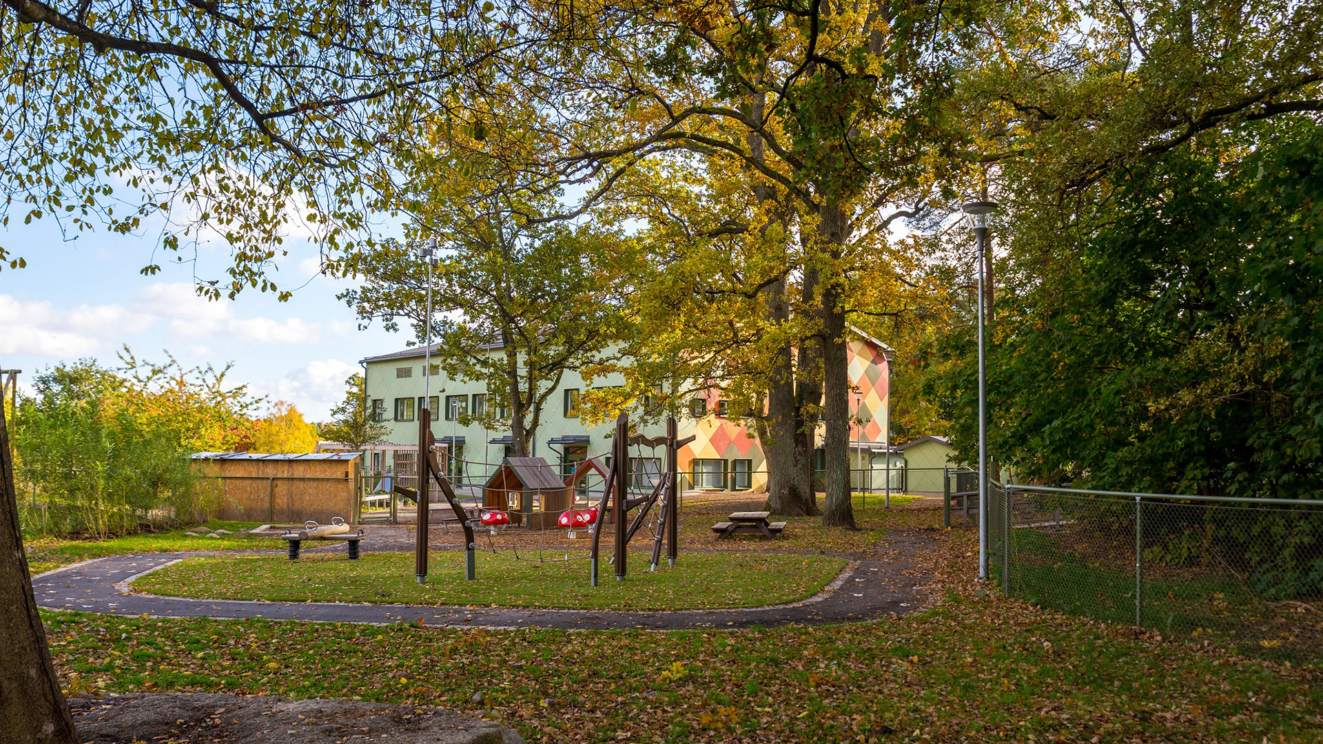 Lekplats i en grönskande miljö framför ett tvåplanshus.
