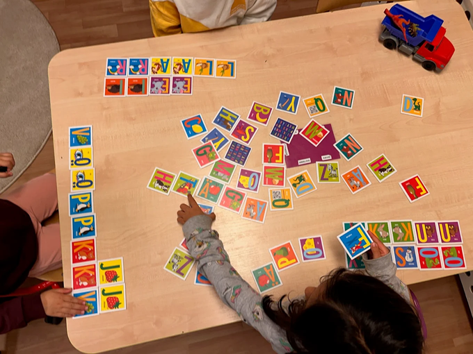 Tre barn sitter vid ett bord och spelar ett bokstavsspel.