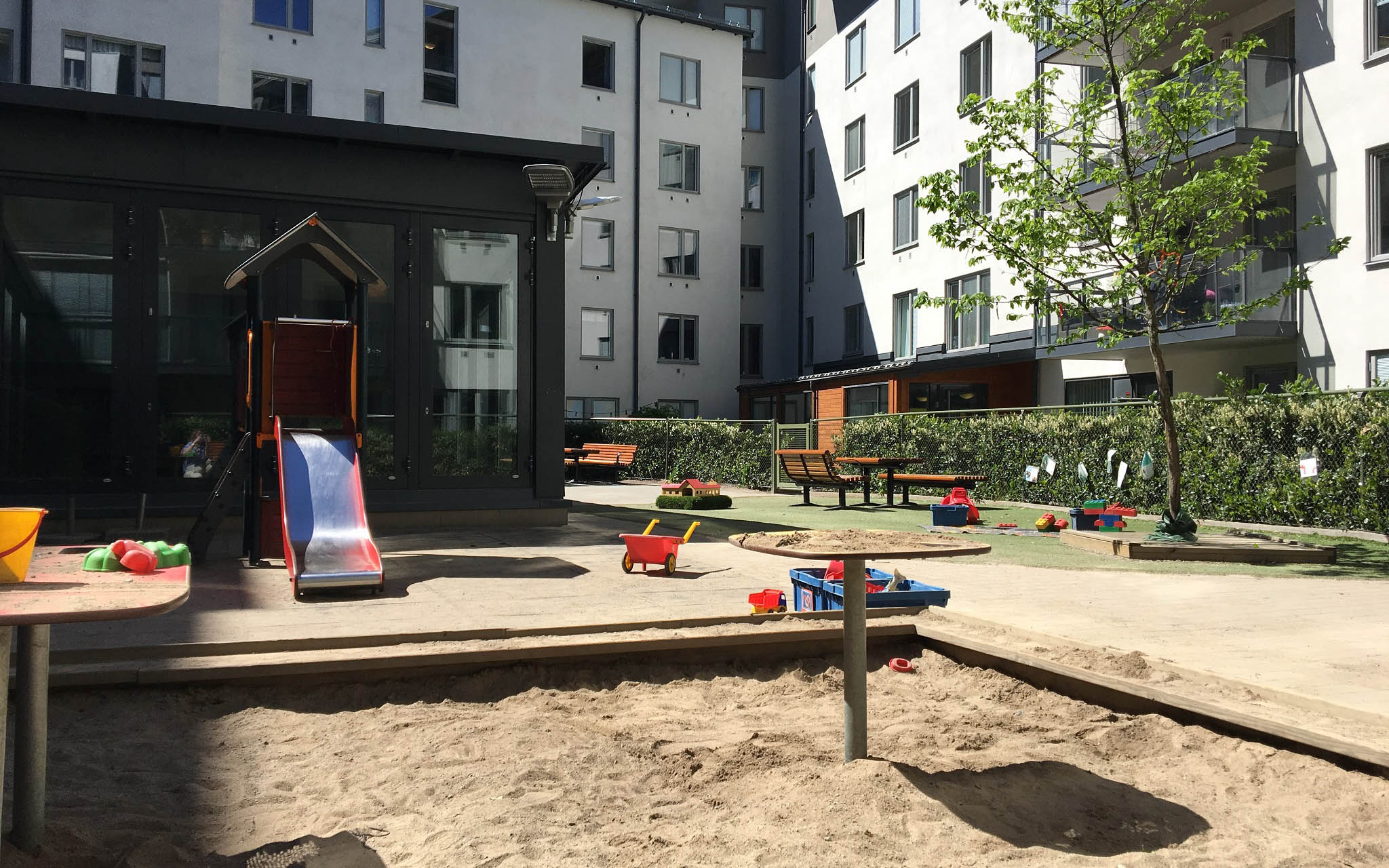 Utemiljö med gård, sandlåda och rutschkana. Ljusa flerbostadshus i bakgrunden.