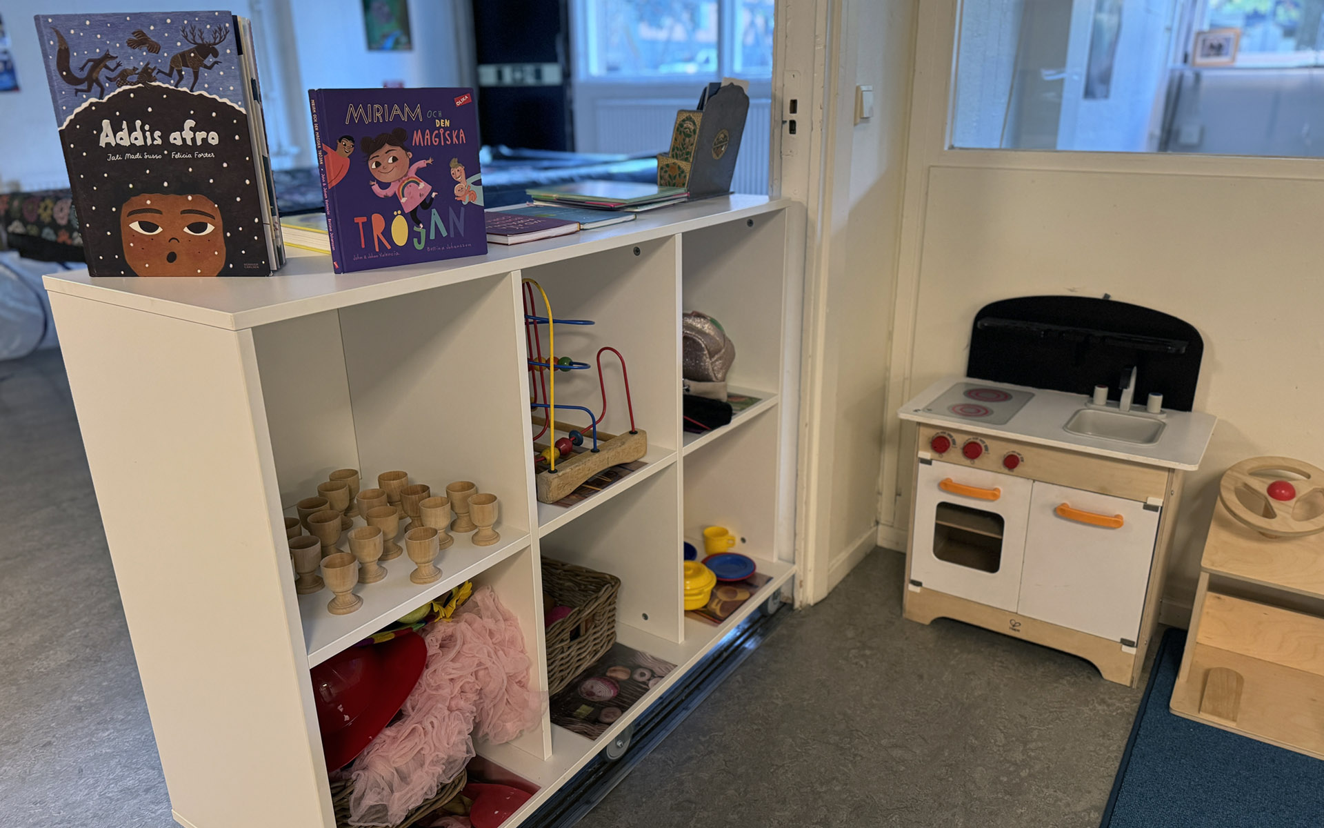 En lekhörna med en leksakspis och hyllor med leksaker och böcker.