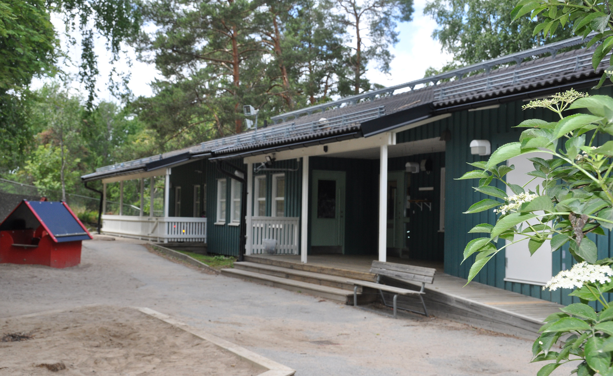 En låg träbyggnad med stort skogsparti framför och en rutschkana.