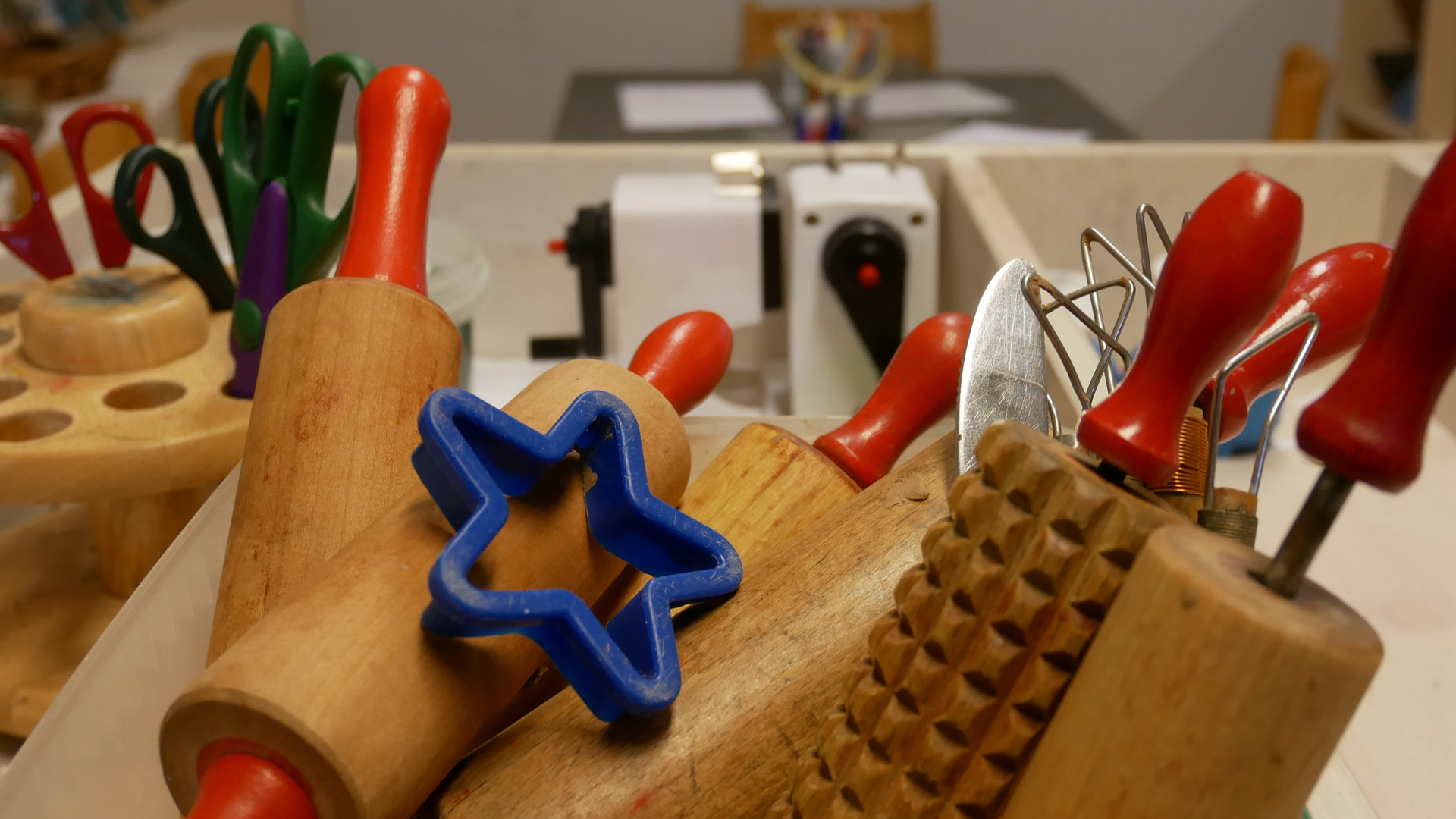 Pedagogiskt lekmaterial i trä och plast, kavlar och saxar på ett bord i en förskolemiljö.
