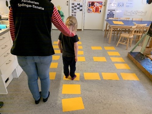 barn och pedagog som går på gula markeringar i golvet