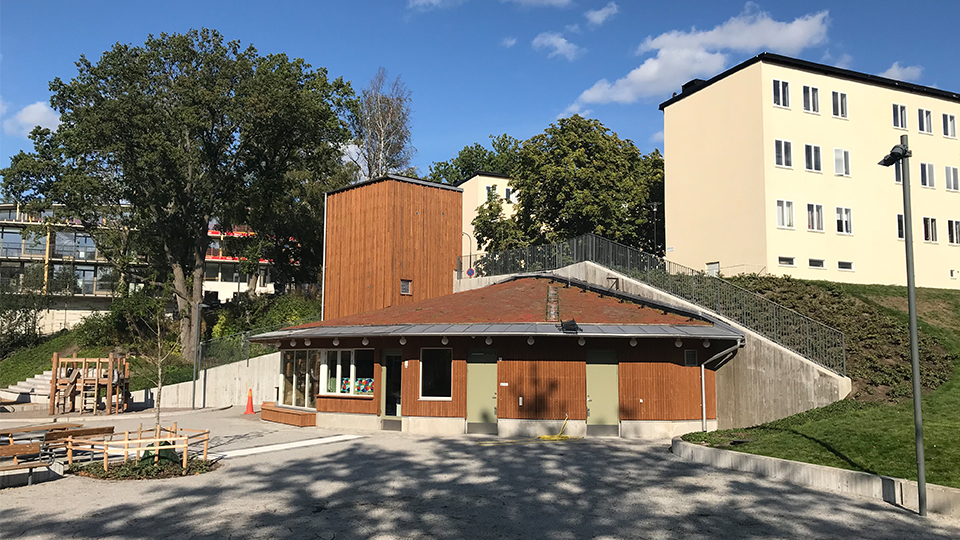 Exteriörbild av öppna förskolan Hjortgläntan, ett lågt hus med sedumtak och lekplats utanför.