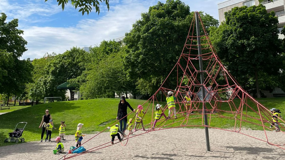 Lekplats i ett grönområde med stor klätterställning och lekande barn.