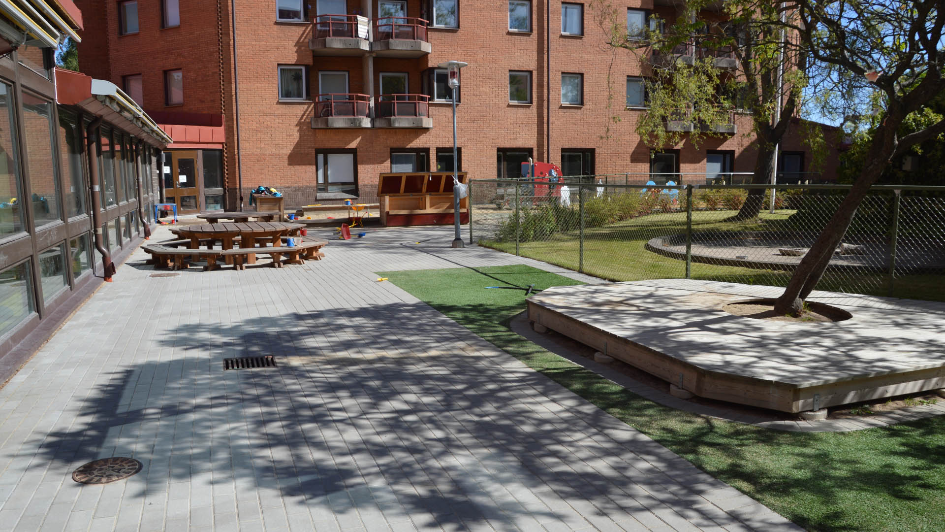 Utemiljö med stor altan intill ett rött tegelhus i flera våningar.