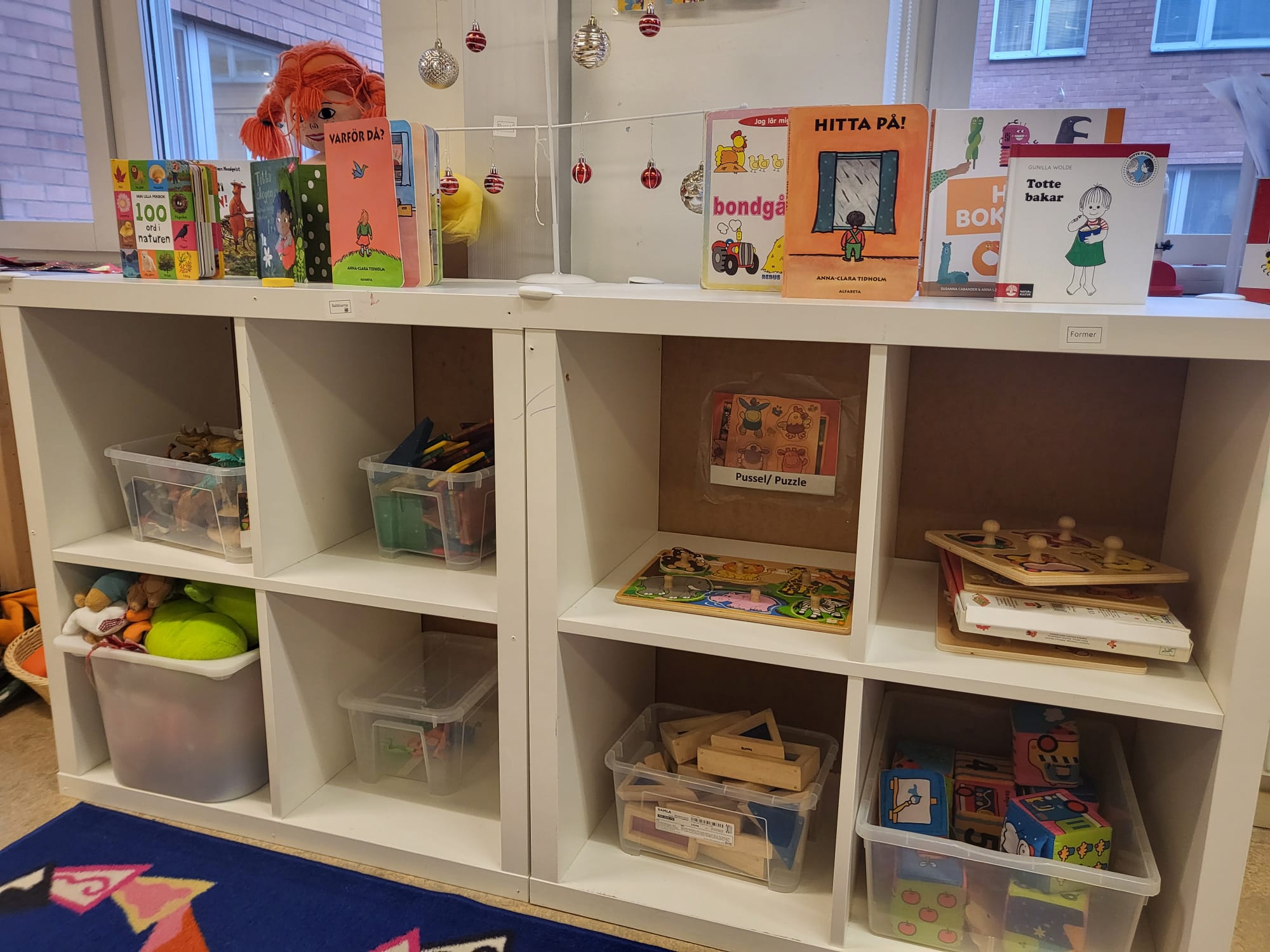 En bokhylla fylld med spel och platsbackar med leksaker och små böcker i. 