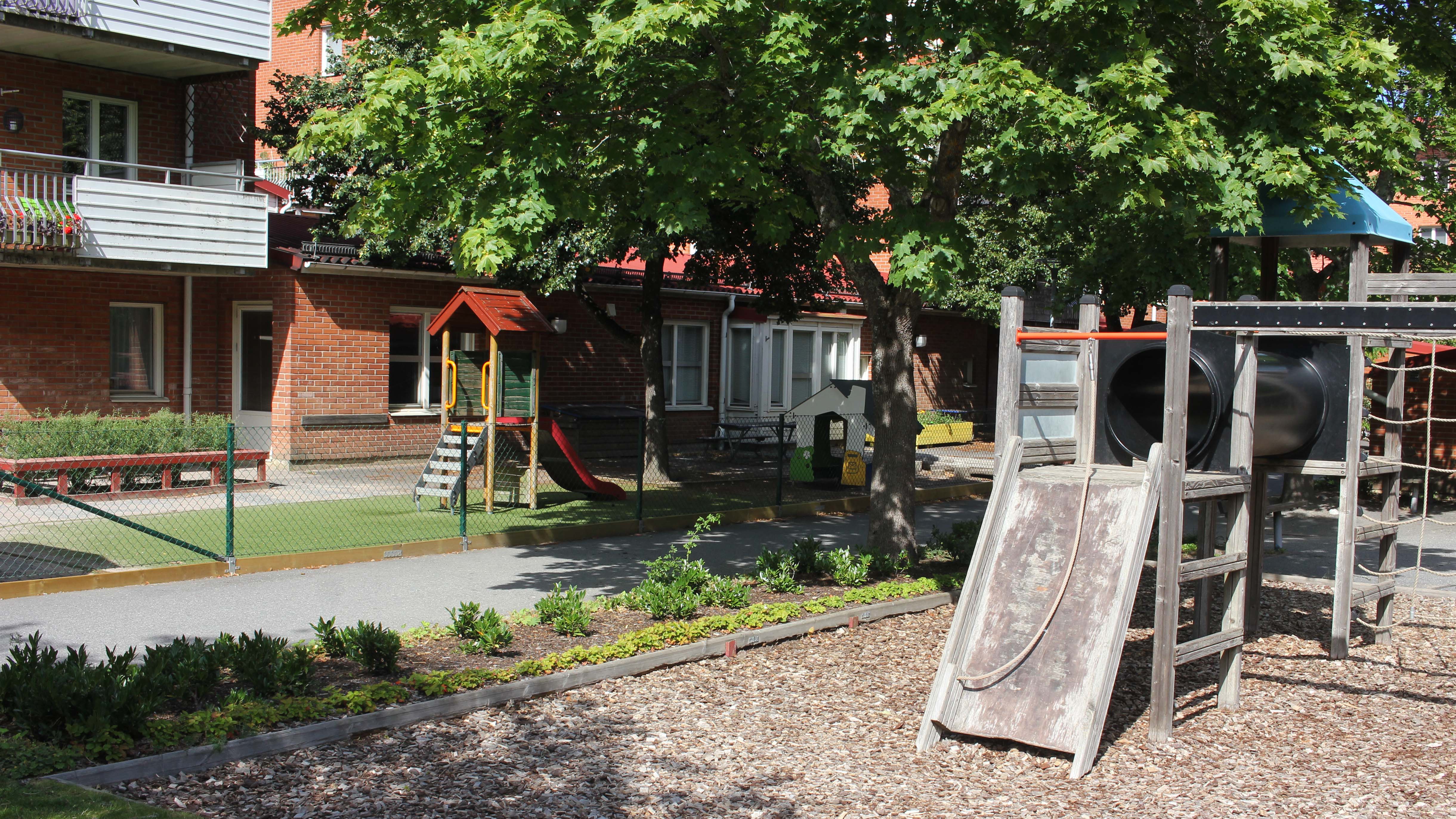 En klätterställning i trä står framför ett flerfamiljshus i tegel med en förskola på bottenplan. 