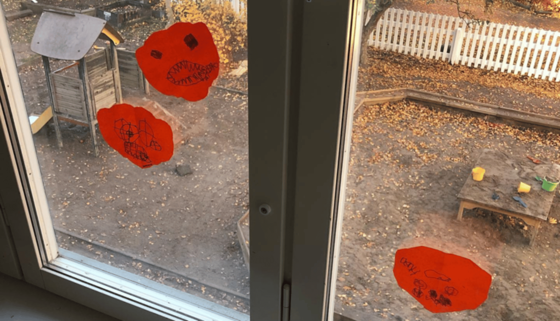Teckningar på ett fönster i förskolans inomhusmiljö med utsikt mot sandlåda och lekplats.