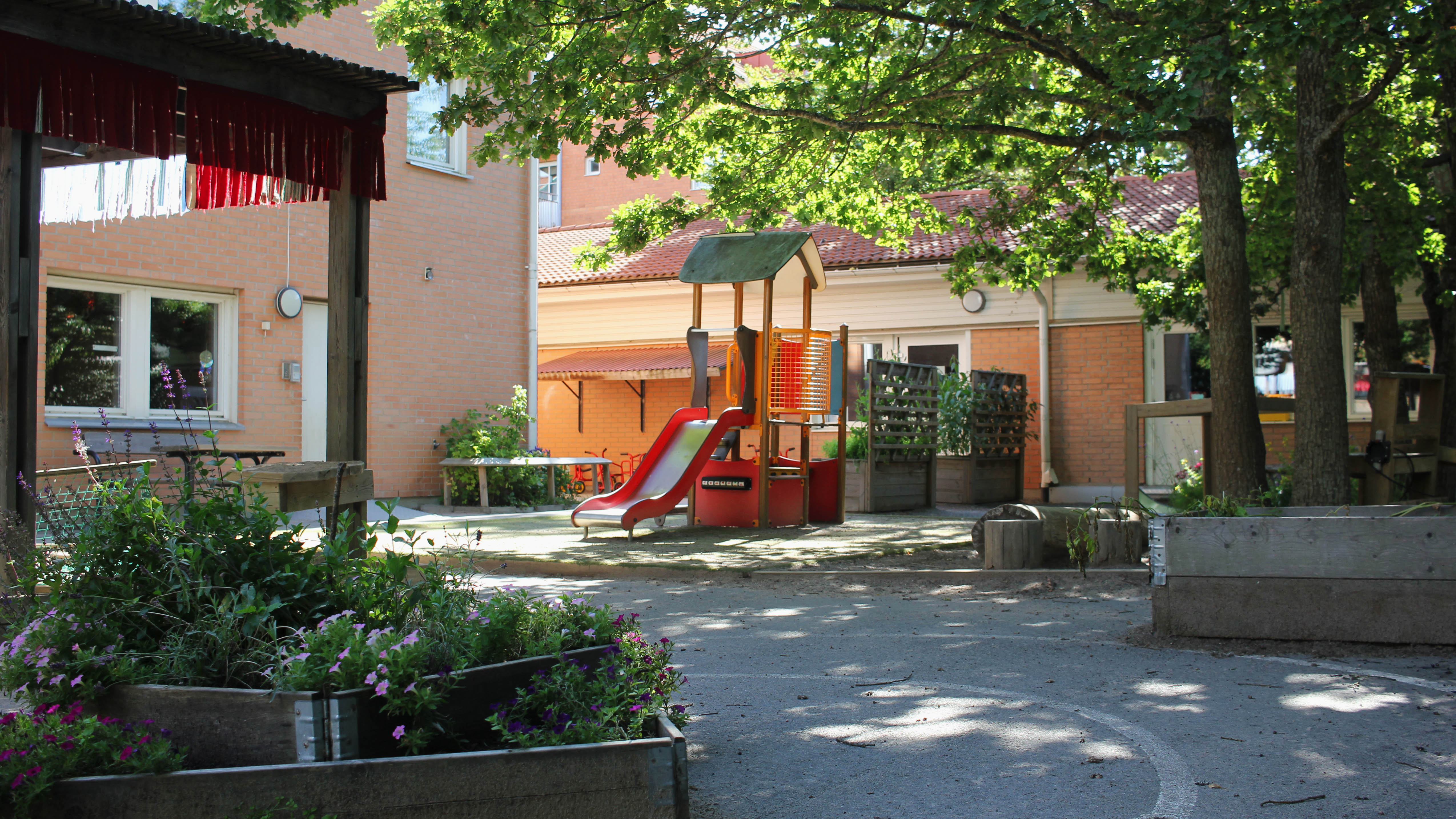 Förskolan Skogsgläntans utegård med klätterställning i gult och rött, planteringslåda med blommor i.