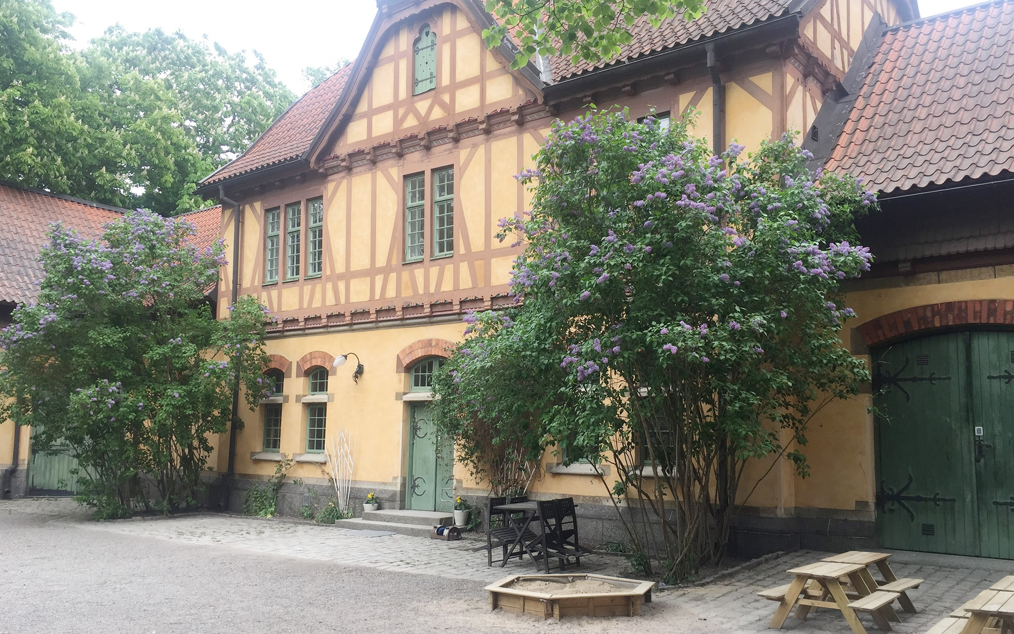 Gult hus med syrener, sandlåda och bänkar utanför.