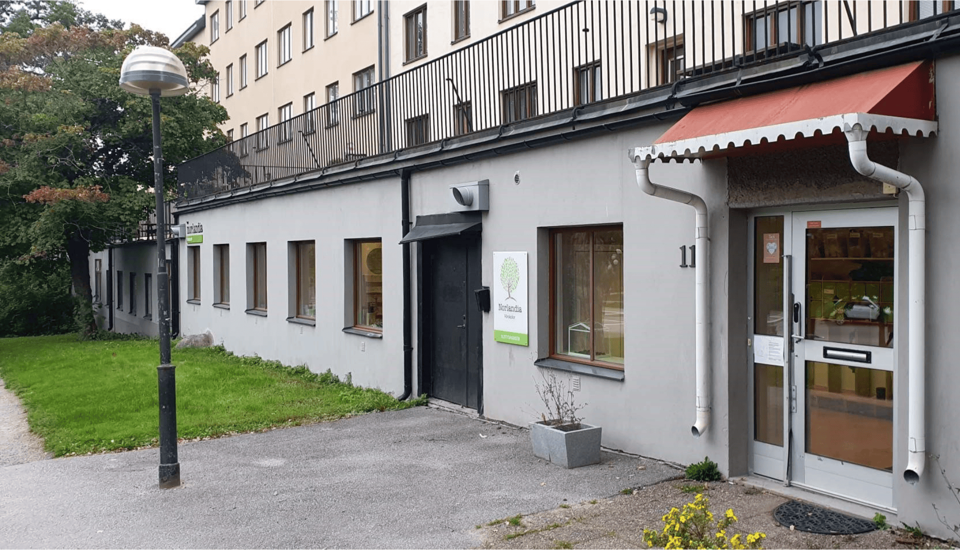 Förskolebyggnad med skylt där det står "Norlandia", entré och fönster mot gatan.