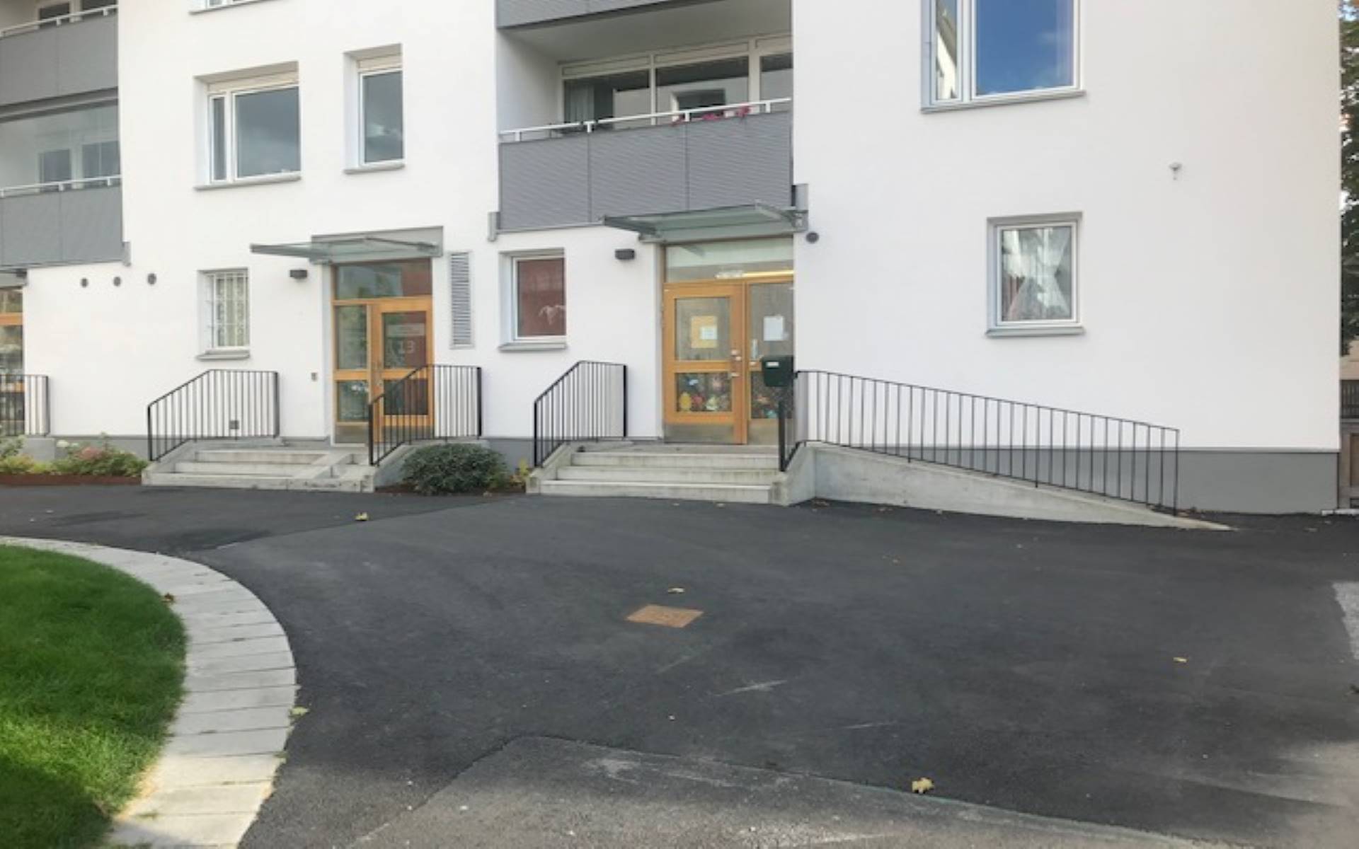 Vitt flervåningshus med asfalt och gräsmatta framför.