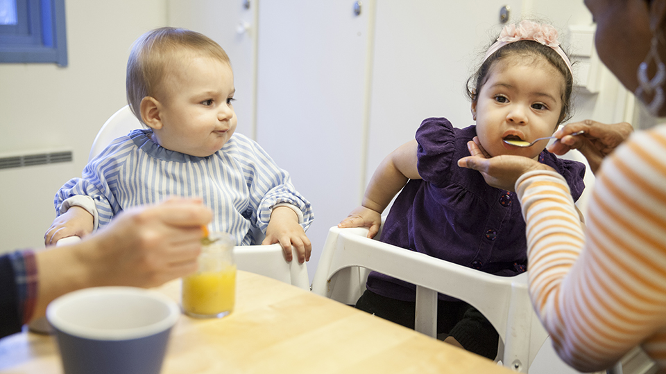 Fotografi, två små barn sitter i barnstol och blir matade.