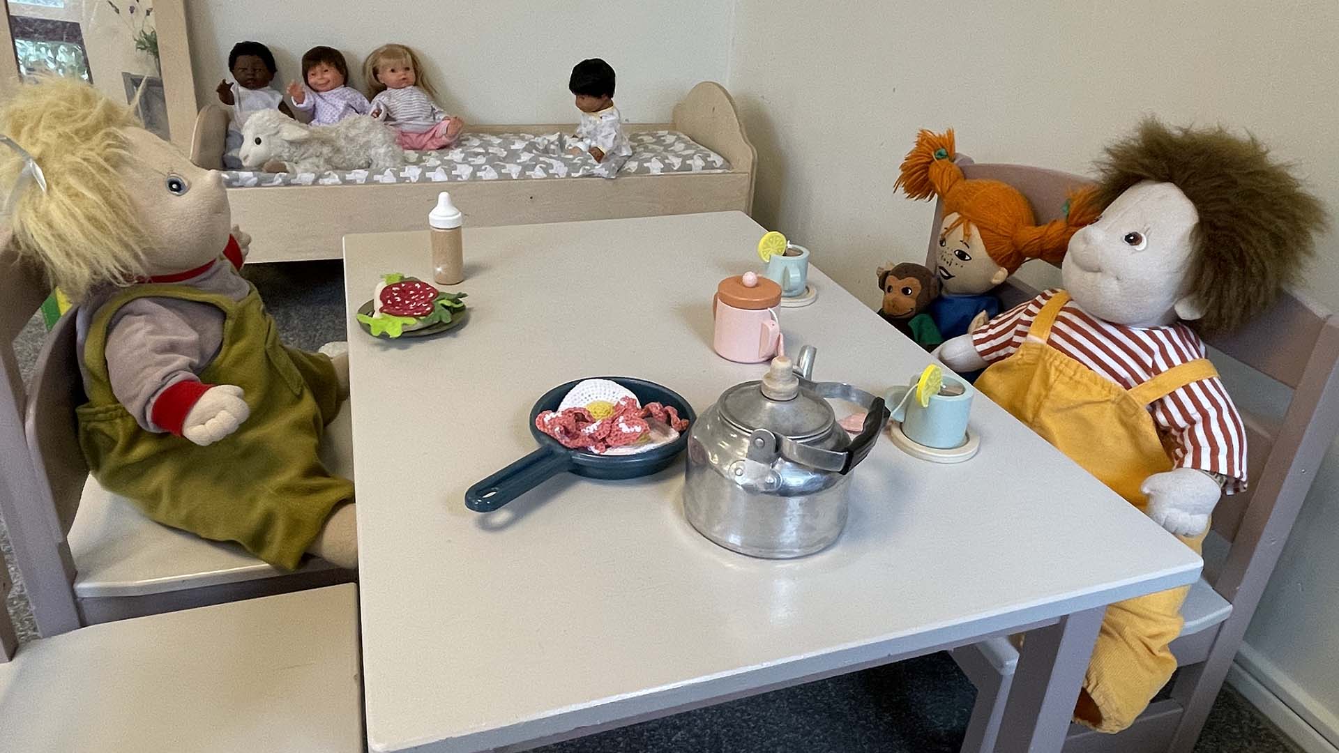 Dockor som sitter vid ett dukat leksaksbord, foto.