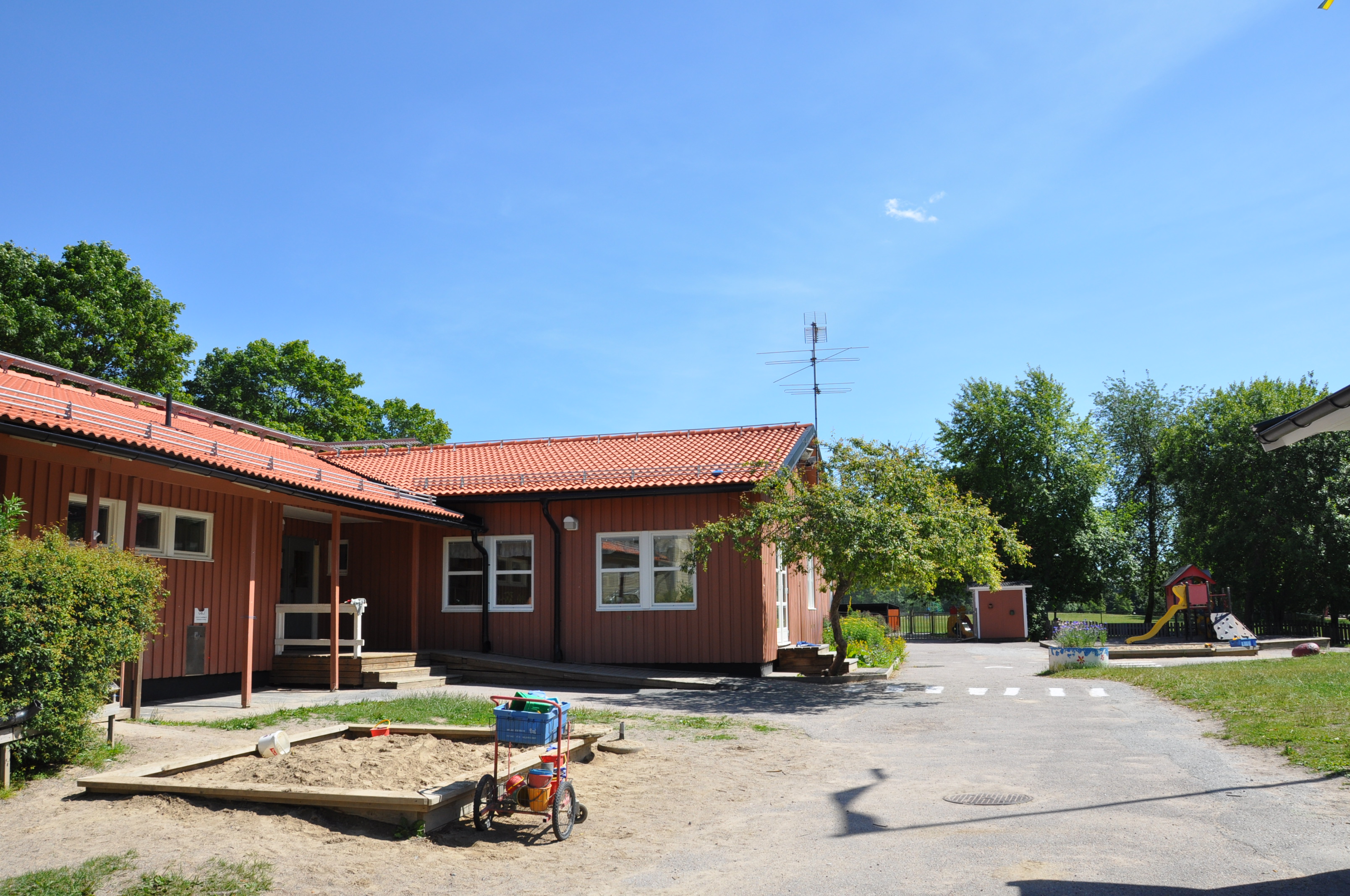 Solig gård framför ett enplanshus, lekredskap och sandlåda.