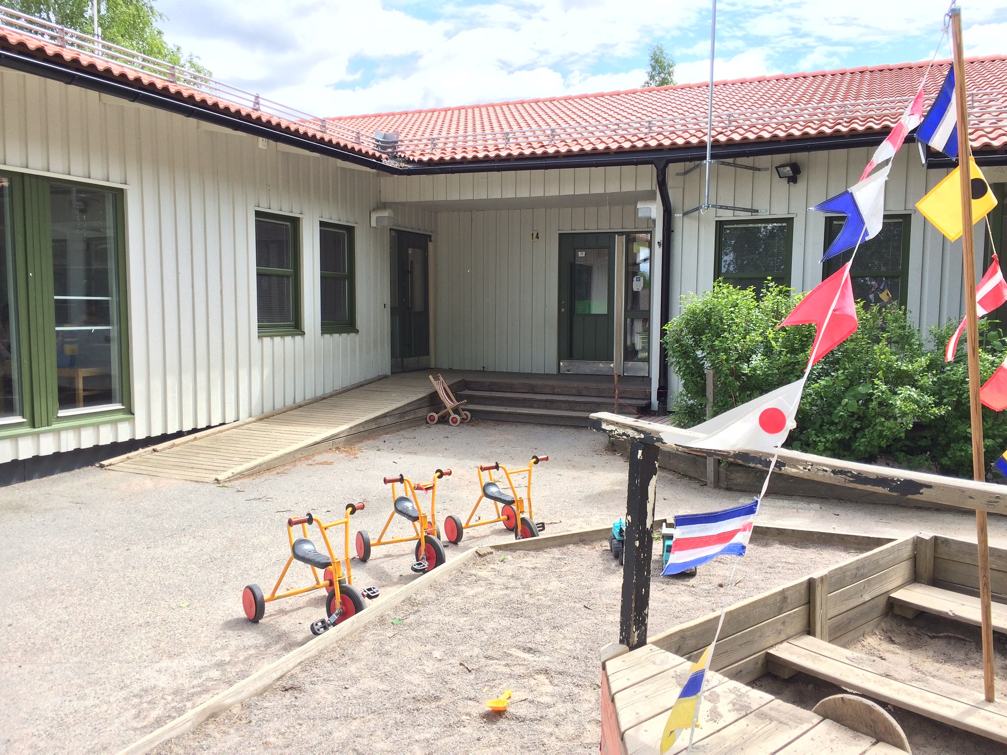Huvudentré till ett enplans trähus, en sandlåda med ett lekredskap i form av en båt på gården.