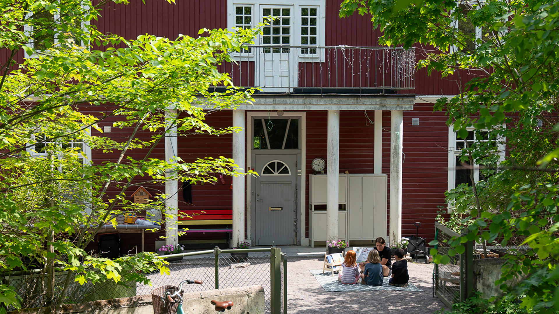 En husentré och en grupp barn som sitter utanför på en filt.