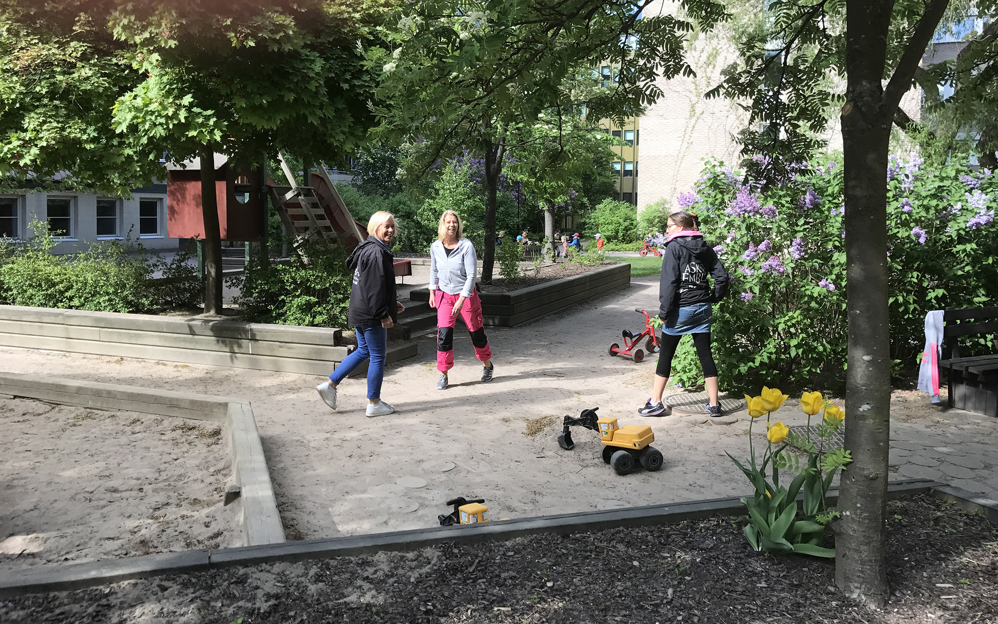 Förskolans gård, sandlåda, träd, blommor, människor.