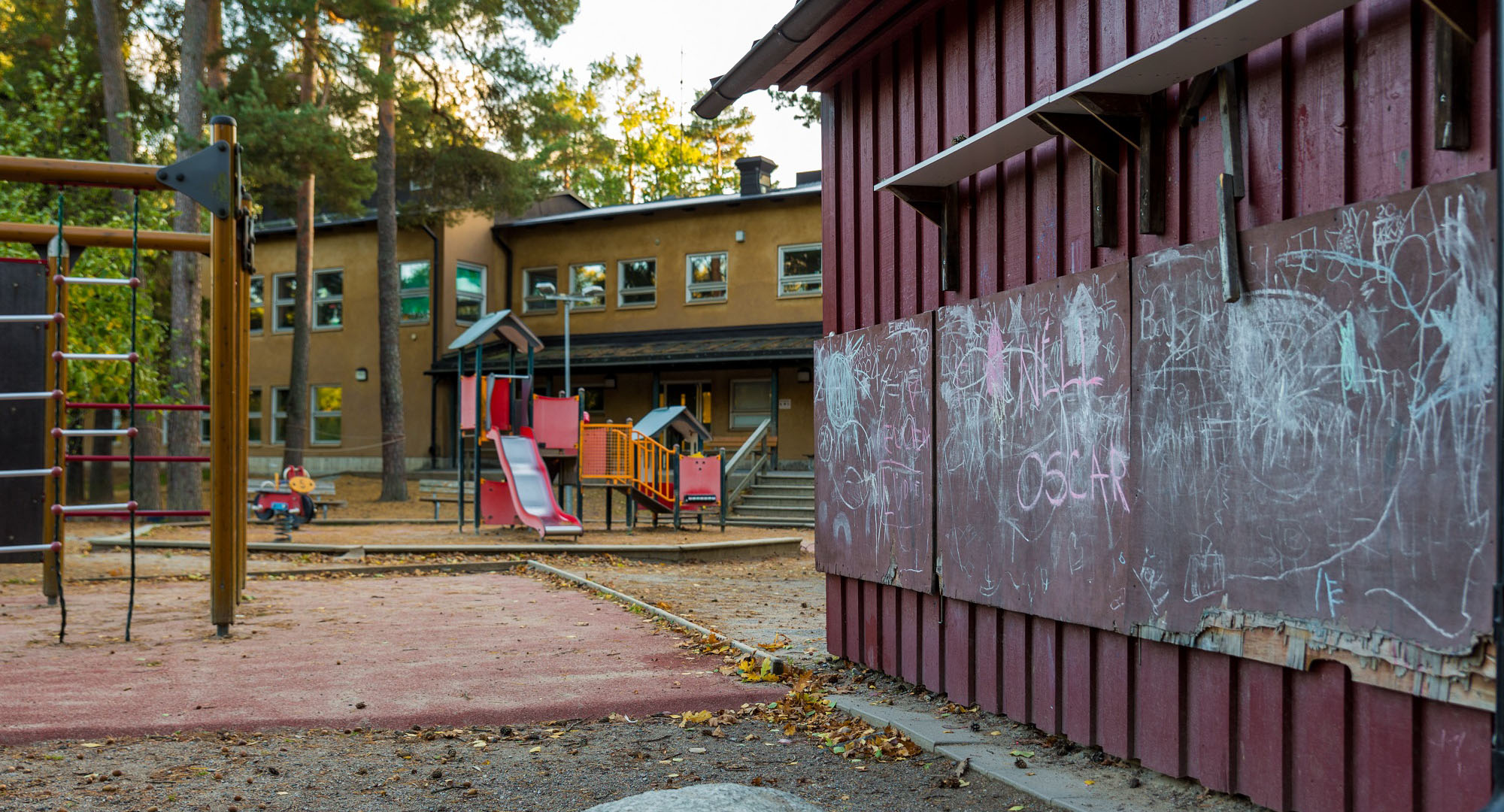 Avståndsbild beigebrun byggnad med lekplats i förgrunden, foto.