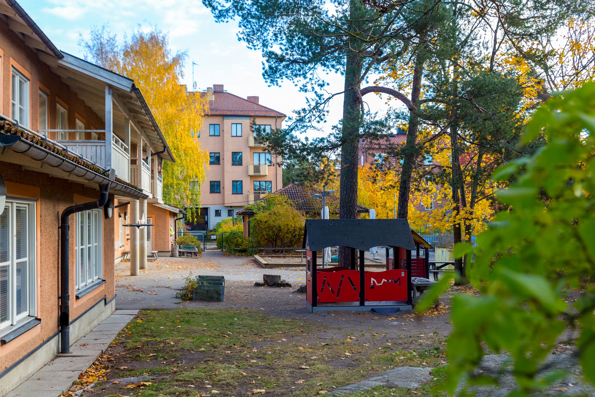 Gård med lekhus och träd framför en byggnad