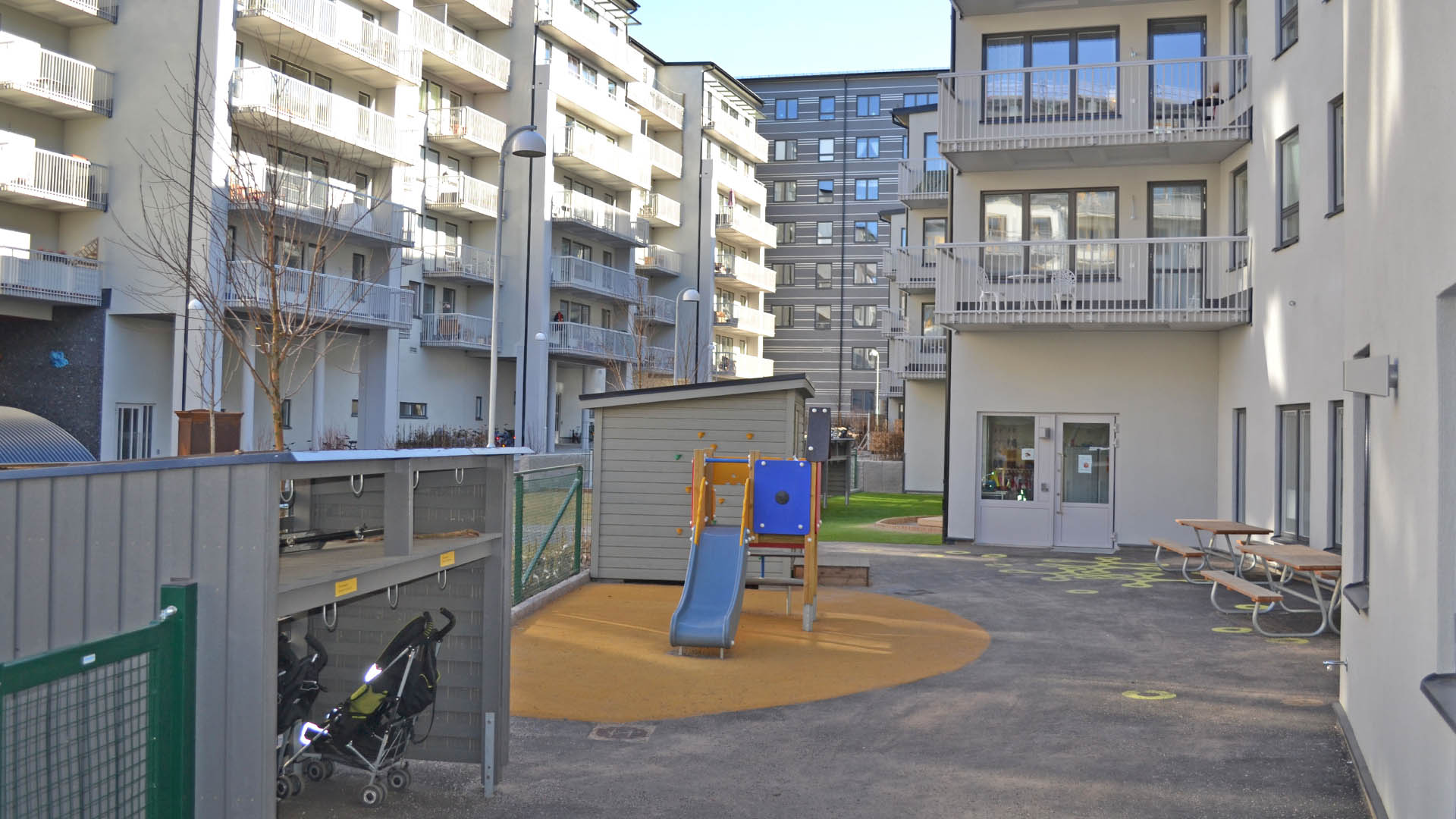 Utemiljö med lekytor och klätterställning och rutchkana. Vita flerbostadshus runtom gården.