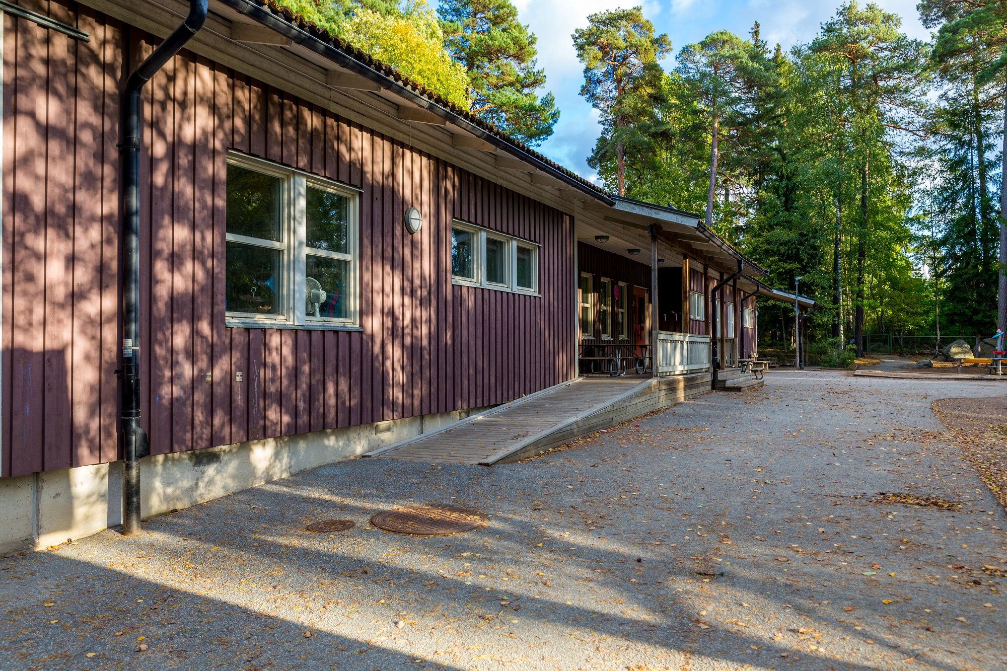 Byggnad med asfalt framför sig och skog i bakgrunden