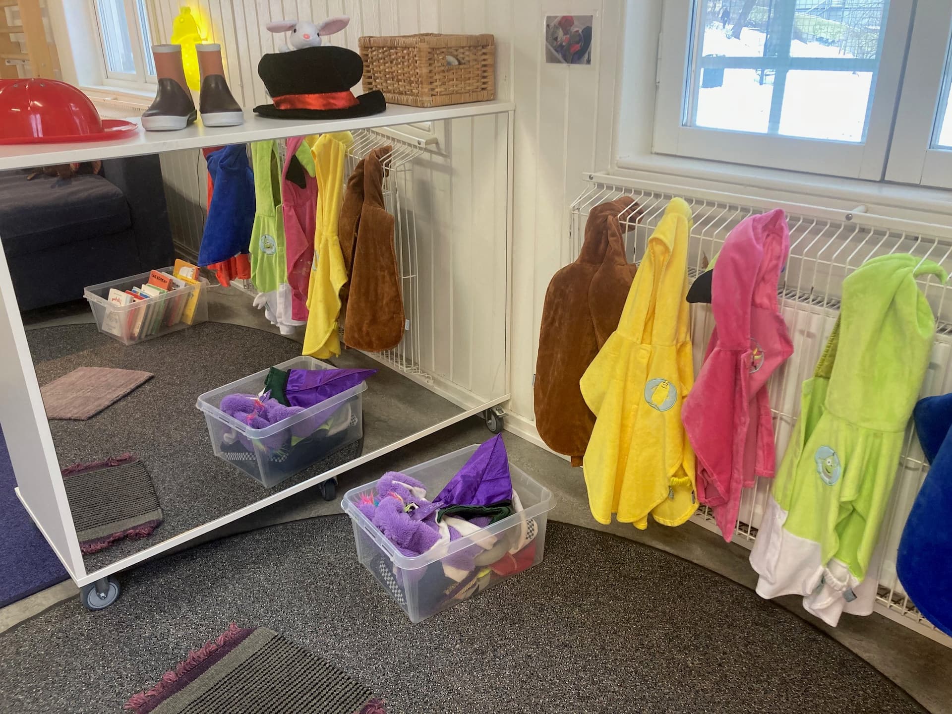 Klädhörna på en förskola med färgglada utklädningskläder, hattar och stövlar på ställningar och i lådor.