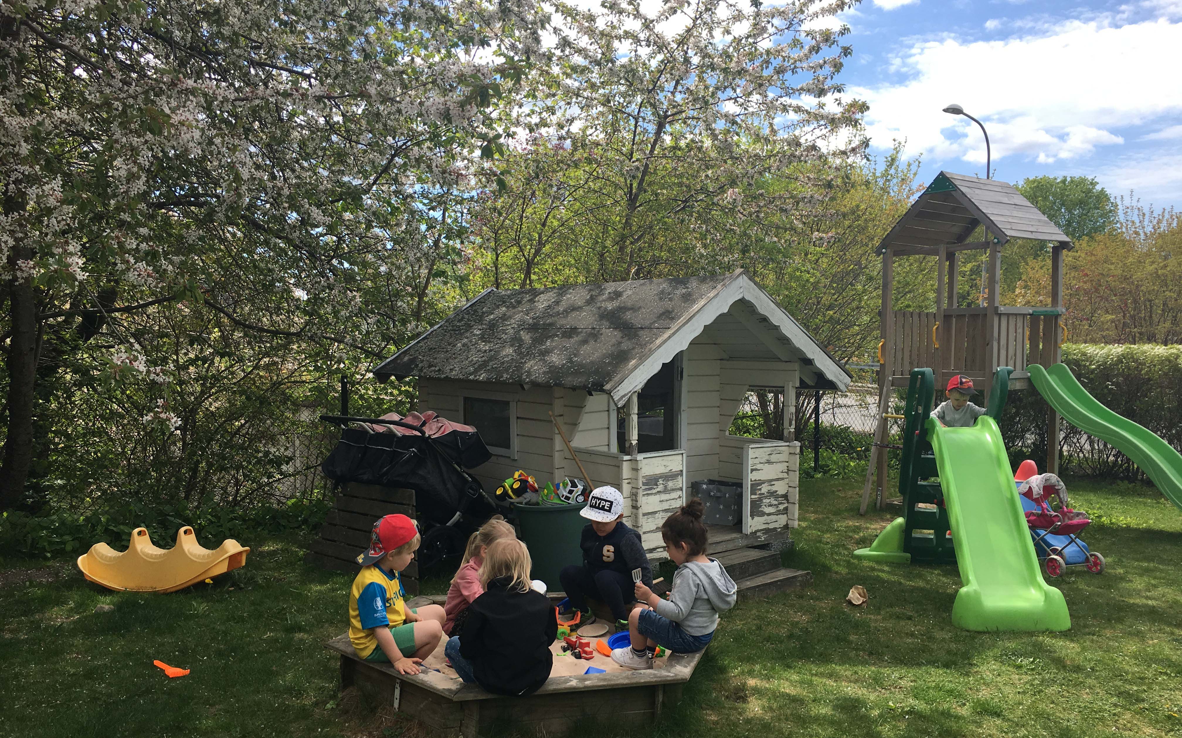 Barn, sandlåda, lekstuga, blommande träd.