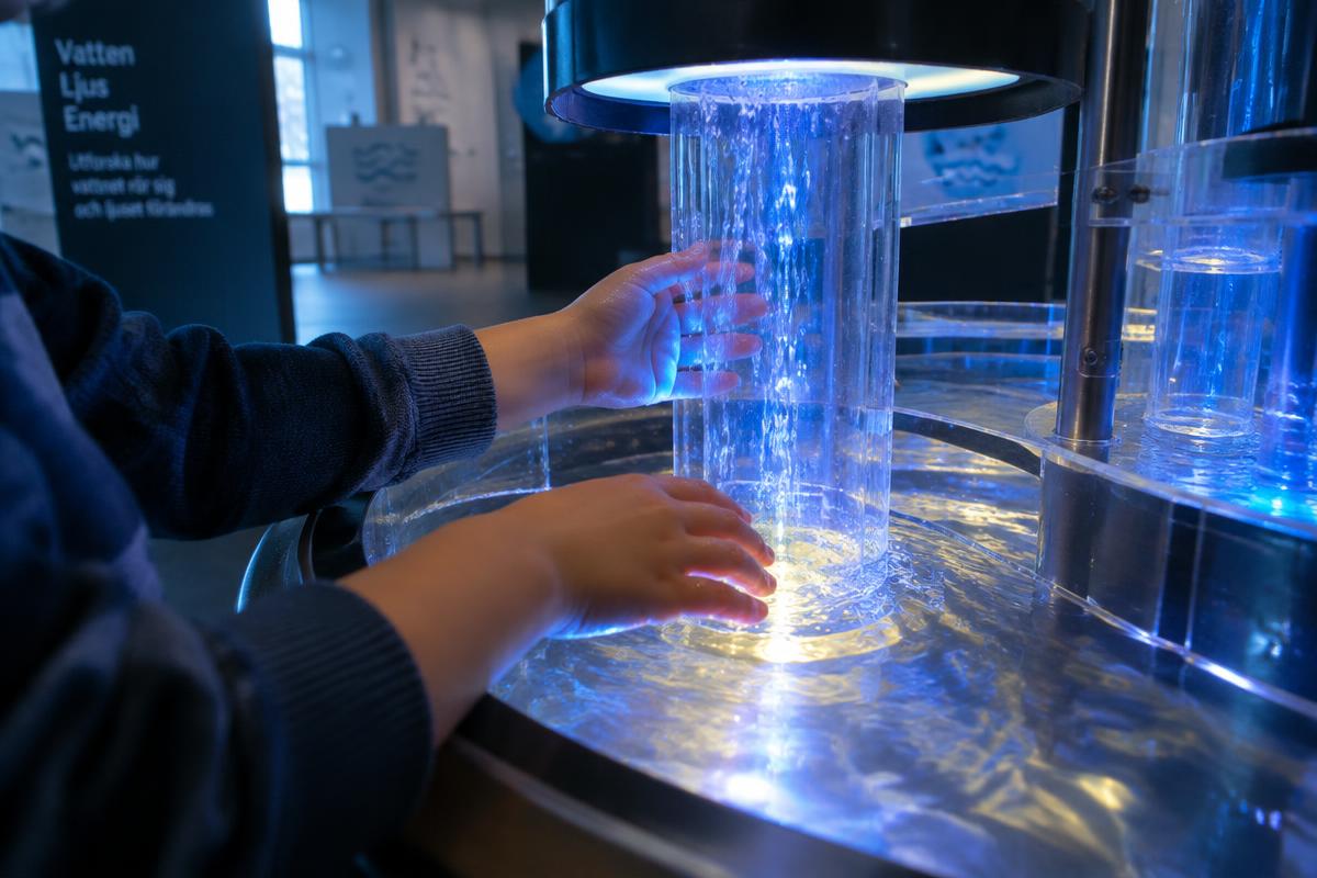 A child's hands exploring a glowing water exhibit at a science centre