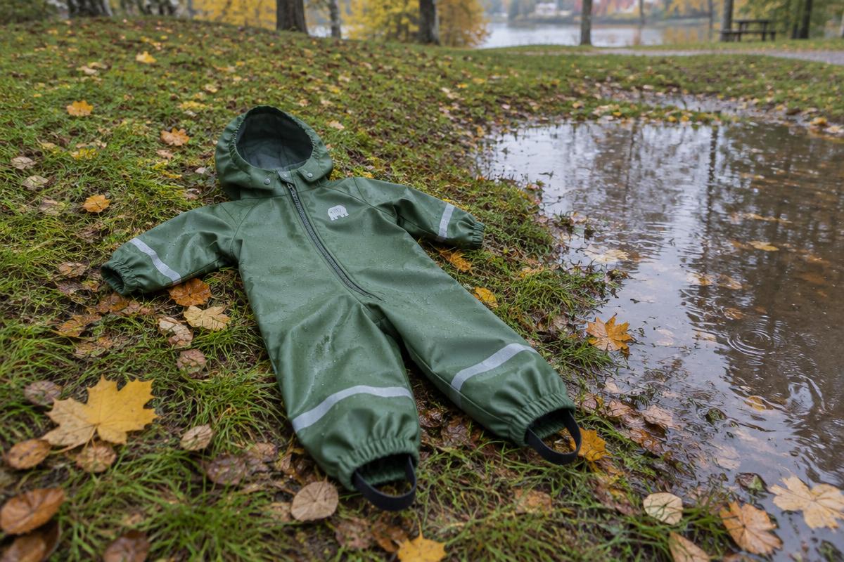 En liten grön regnoverall i ett stycke på blött gräs bredvid en höstpöl